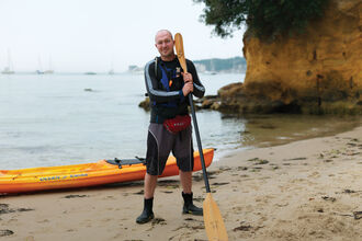 Dan stands on a beach with his kayak