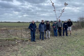 A group of volunteers stand in front of a hedge they have laid