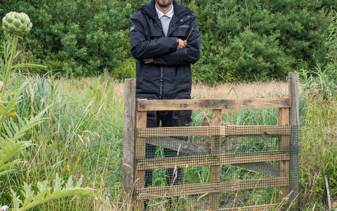 John stands besides a gate on a reserve