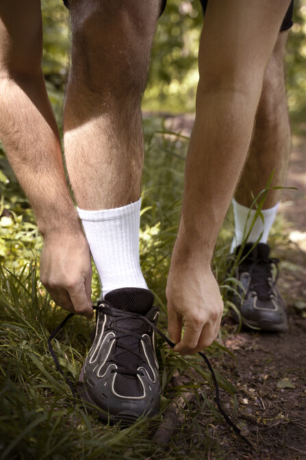 A mans hands are shown lacing up a running trainer in a woodland trail